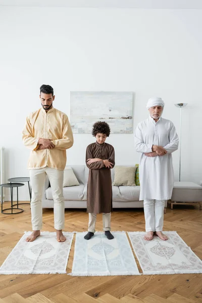 Multiethnische Männer und arabischer Junge beten zu Hause auf Teppichen — Stockfoto