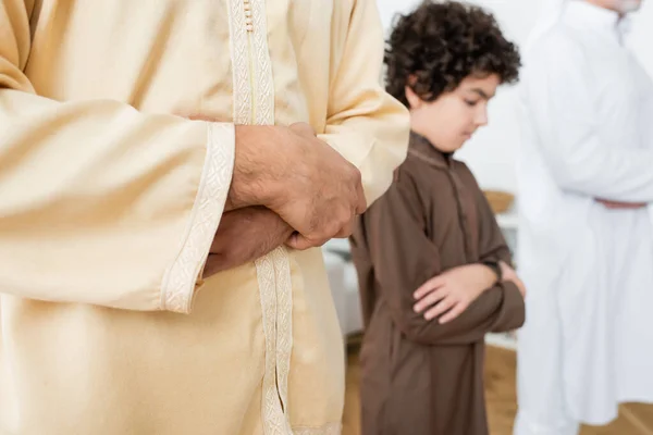 Hombre joven musulmán rezando cerca de un hijo borroso en casa - foto de stock