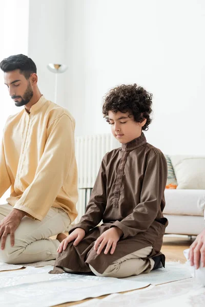 Lockiges muslimisches Kind betet auf Teppich neben Vater und Opa zu Hause — Stockfoto