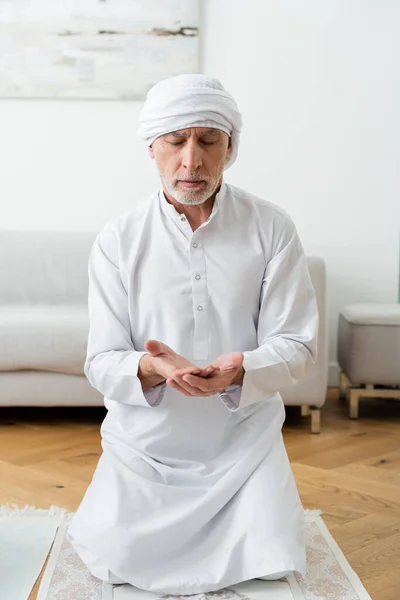 Mature man in traditional muslim clothes praying at home — Stock Photo