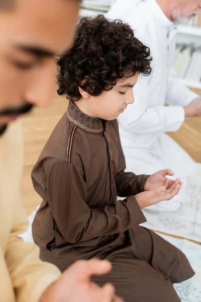 Bouclé arabian garçon priant près de père et grand-parent à la maison — Photo de stock