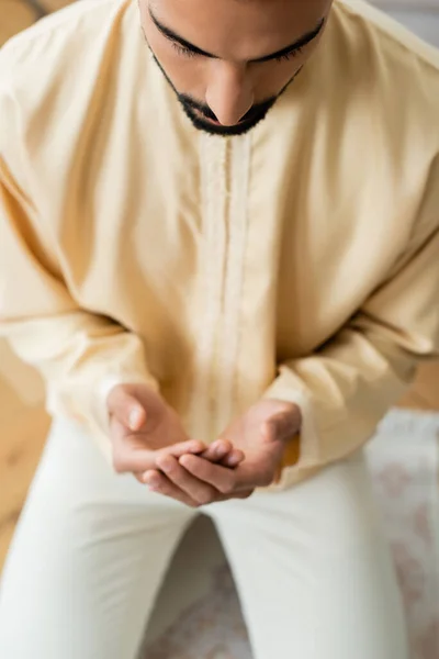 Vista ad alto angolo del giovane arabo che prega sul tappeto sfocato a casa — Foto stock