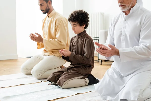 Preteen arabian boy praying near men at home — Stock Photo