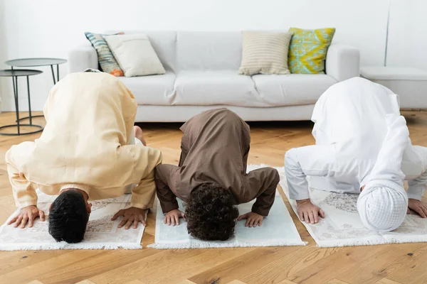 Arabian men and boy bending on rugs while praying at home — Stock Photo