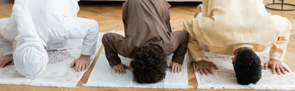 Muslimische Männer und Kinder beugen sich zu Hause auf traditionellen Teppichen, Banner — Stockfoto