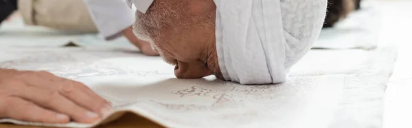 Вид збоку зрілого чоловіка, що молиться на килимі вдома, банер — стокове фото