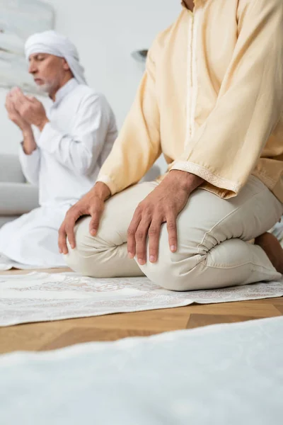 Tiefansicht eines jungen muslimischen Mannes, der auf Teppich neben seinem Vater sitzt und zu Hause betet — Stockfoto