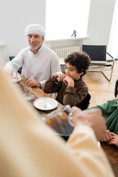 Smiling mature man holding glass near muslim family at home — Stock Photo