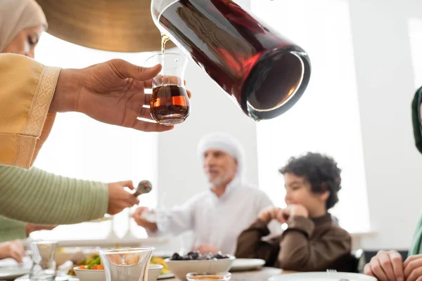 Moslem schenkt Tee in der Nähe verschwommener Familie und Essen zu Hause ein — Stockfoto