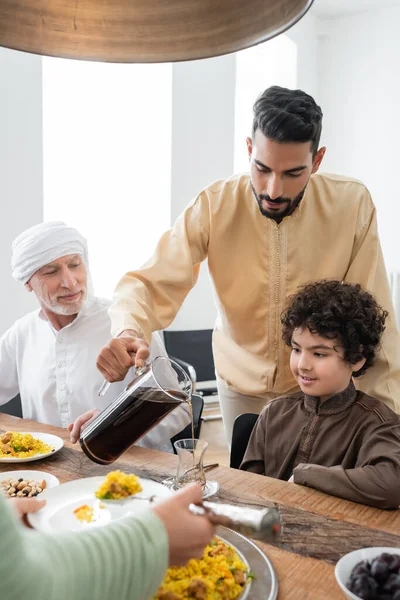 Árabe hombre vertiendo té cerca de hijo y papá en casa - foto de stock