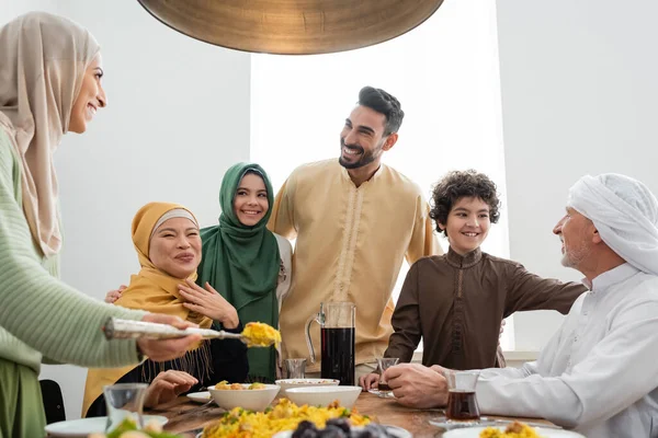 Positivo interracial muçulmano família olhando para mulher servindo pilaf em casa — Fotografia de Stock