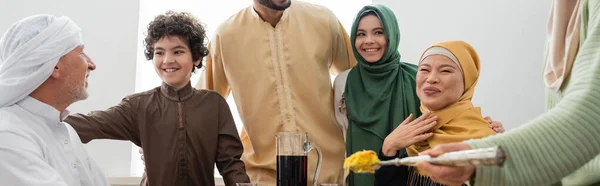 Famille musulmane multiethnique souriante près d'une femme avec pilaf à la maison, bannière — Photo de stock