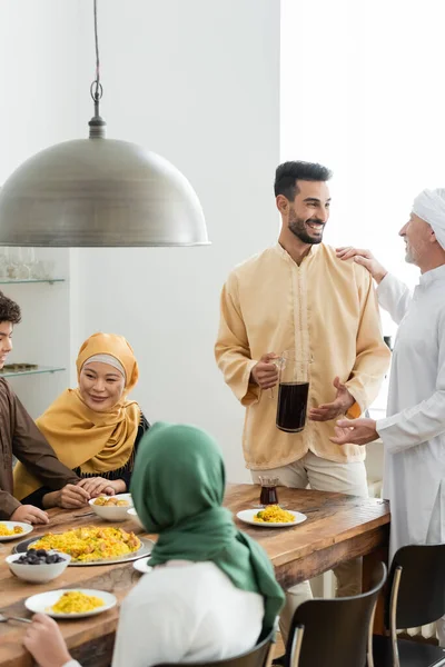 Зрелый мужчина разговаривает с арабским сыном рядом с межрасовой мусульманской семьей и едой дома — стоковое фото