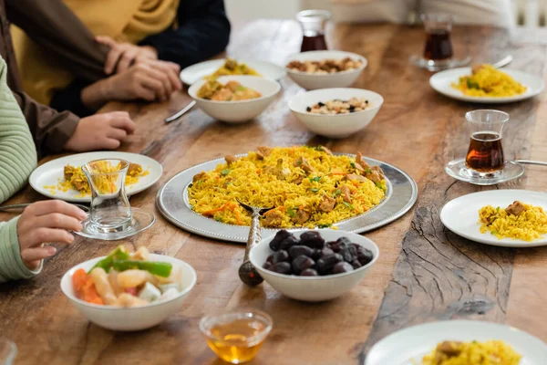 Cropped view of muslim family near table served with pilaf, dates, baklava, tea and honey — Stock Photo