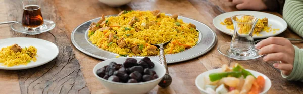 Partial view of muslim woman near pilaf, dates, baklava and tea served on table, banner — Stock Photo