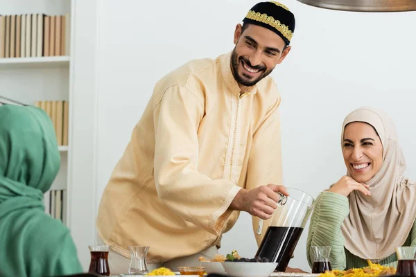 Glücklicher muslimischer Mann mit Totenkopf gießt Tee neben glücklicher Frau im Hijab — Stockfoto