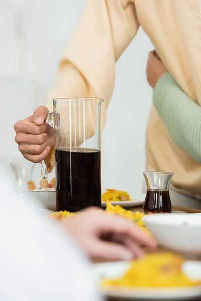 Cropped view of man holding jug with tea during family dinner on blurred foreground — Stock Photo