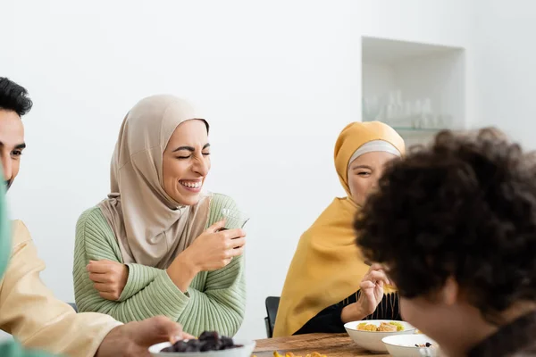 Cheerful muslim woman in hijab laughing during dinner with multicultural family — Stock Photo