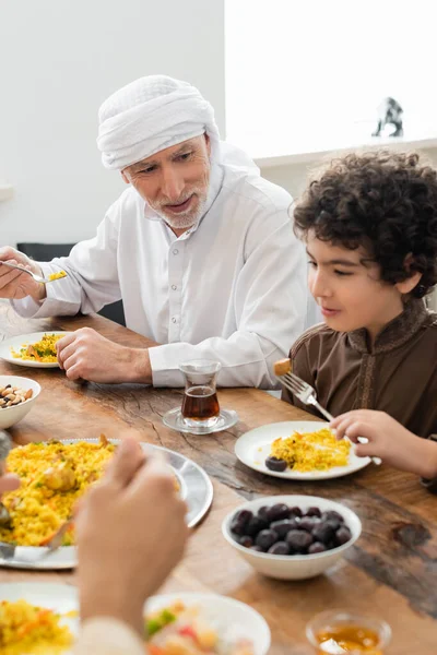 Homem muçulmano comendo pilaf com neto árabe durante o jantar de família — Fotografia de Stock
