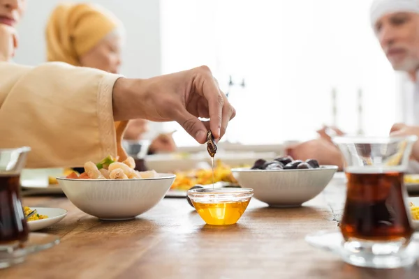 Man dipping date into honey during dinner with multiethnic muslim family — Stock Photo