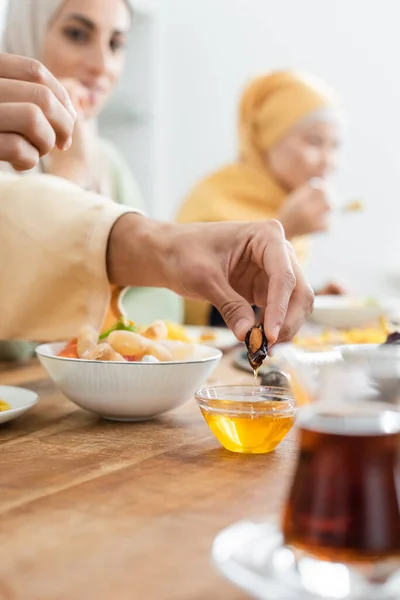 Чоловік занурює дату в мед під час обіду з розмитими міжрасовими мусульманськими жінками — стокове фото