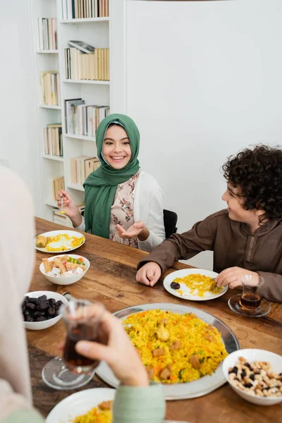 Heureuse fille dans hijab pointant avec la main pendant le dîner avec la famille musulmane — Photo de stock