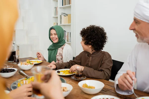 Alegre chica musulmana riendo durante la cena con la familia multiétnica - foto de stock