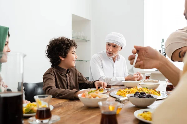 Hombre musulmán cenando con nietos multiétnicos felices y familia borrosa - foto de stock