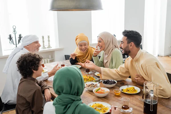 Young arabian man talking to cheerful multicultural muslim family during dinner — Stock Photo