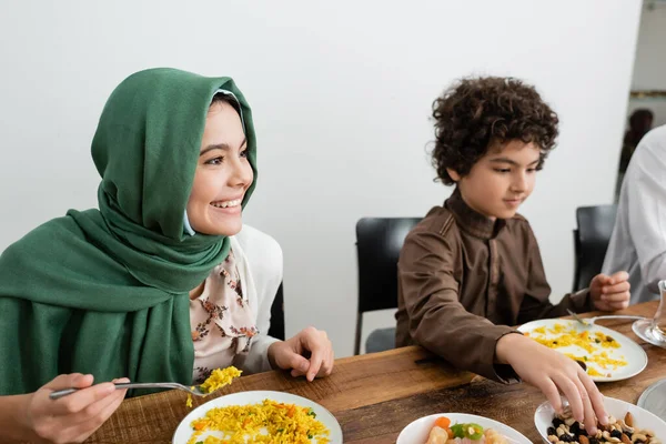 Feliz musulmán chica en hijab comer pilaf cerca árabe hermano - foto de stock