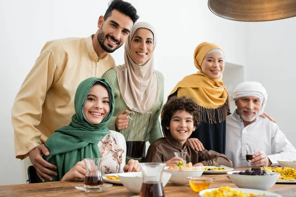 Multicultural muslim family smiling at camera near served pilaf and tea — Stock Photo