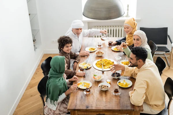 Vista de ángulo alto de la familia musulmana multiétnica feliz cenando en casa - foto de stock