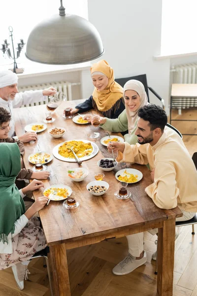 Vista de ángulo alto de hombre maduro verter té cerca de la familia musulmana multicultural cenar en casa - foto de stock