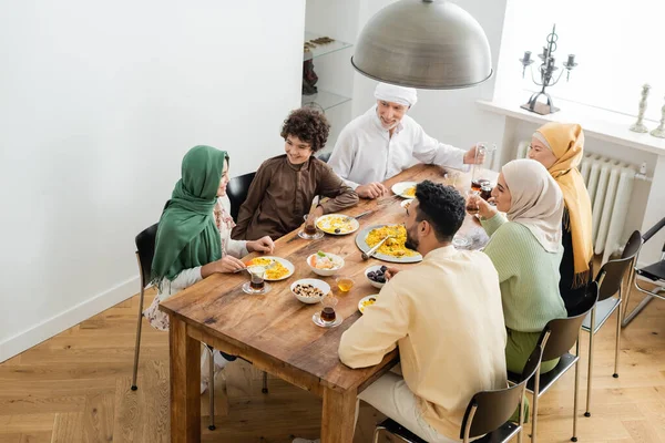 Vista de ángulo alto de la familia musulmana interracial sonriendo durante la cena en casa - foto de stock