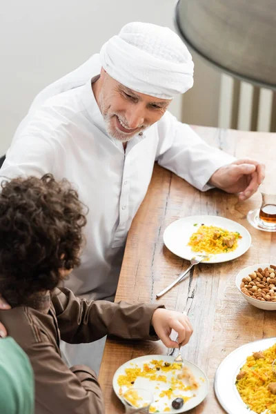 Mature muslim man in turban having dinner with arabian grandson at home — Stock Photo