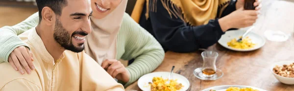 Joven árabe sonriendo durante la cena con la familia musulmana, pancarta - foto de stock
