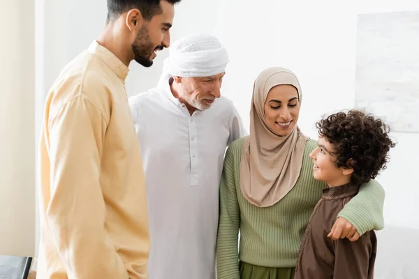 Lächelnde muslimische Frau umarmt arabischen Sohn in der Nähe von Vater und Ehemann — Stockfoto