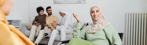 Mulher muçulmana feliz falando com mãe turva perto de família interracial em casa, banner — Fotografia de Stock