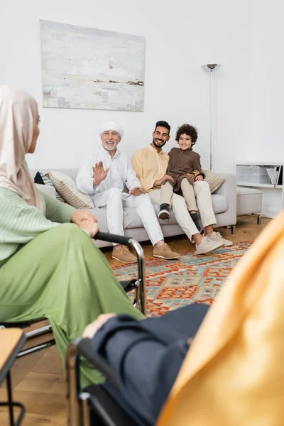 Зрелый мусульманин машет рукой, разговаривая с мультикультурной семьей в гостиной — стоковое фото