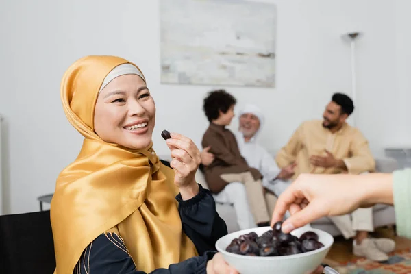 Happy asian woman in hijab holding dates near daughter and interracial muslim family on blurred background — Stock Photo
