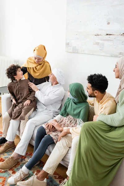 Hombre maduro hablando con nieto árabe cerca de la esposa y la familia musulmana multicultural - foto de stock