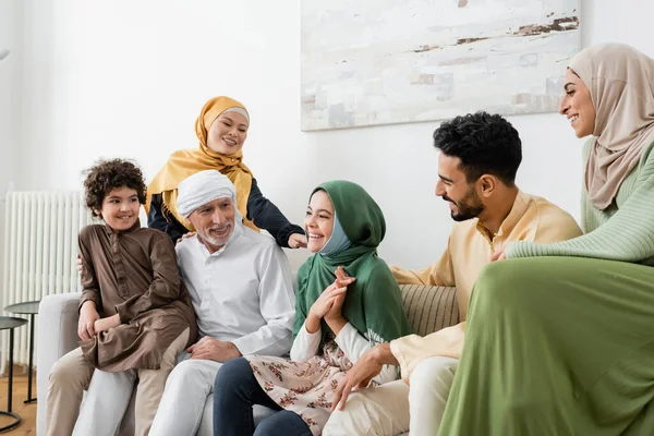 Happy multicultural muslim family looking at smiling girl while sitting on couch at home — Stock Photo