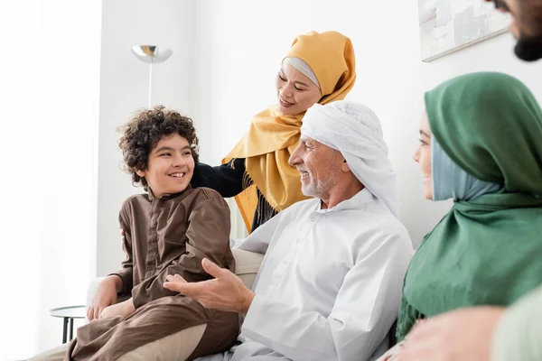 Maduro musulmán hombre en turbante hablando con árabe nieto cerca feliz interracial familia - foto de stock