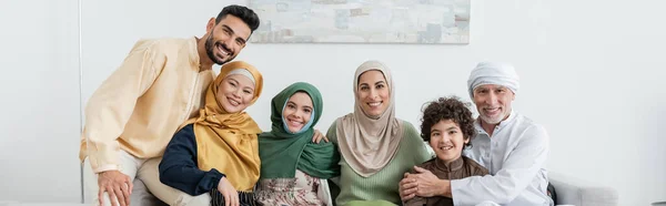 Alegre familia musulmana multicultural mirando a la cámara en casa, pancarta - foto de stock