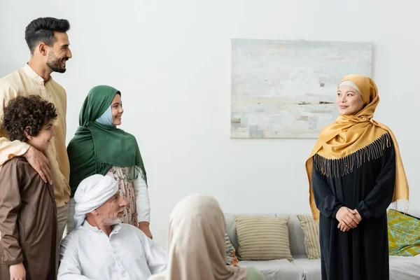 Усміхнена азіатська жінка в хіджабі дивиться на багатоетнічну мусульманську сім'ю вдома — стокове фото