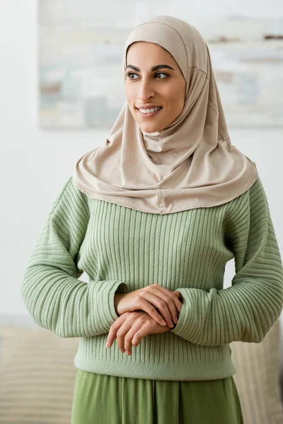 Glückliche muslimische Frau im Hidschab lächelt, während sie zu Hause wegschaut — Stockfoto