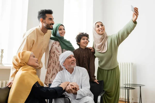 Счастливая арабская женщина делает селфи на смартфоне с мультикультурной мусульманской семьей — стоковое фото