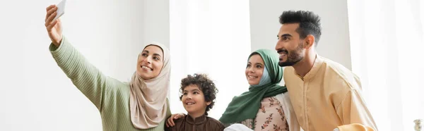 Femme musulmane souriante prenant selfie sur smartphone avec famille interracial, bannière — Photo de stock