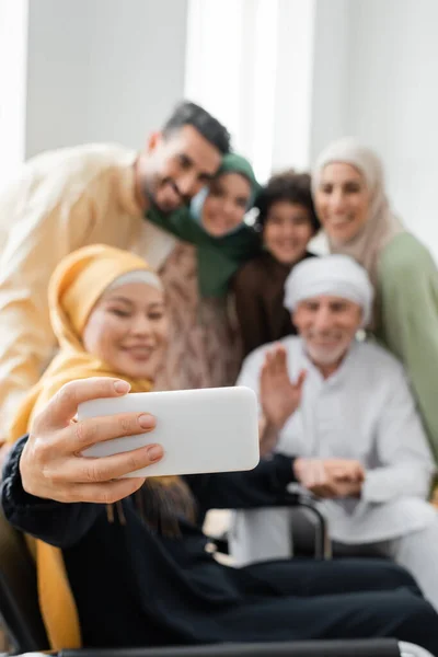 Happy asian woman taking selfie with blurred interracial muslim family — Stock Photo