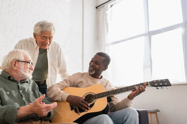 Lächelnder afrikanisch-amerikanischer Mann spielt Akustikgitarre bei Freunden zu Hause — Stockfoto